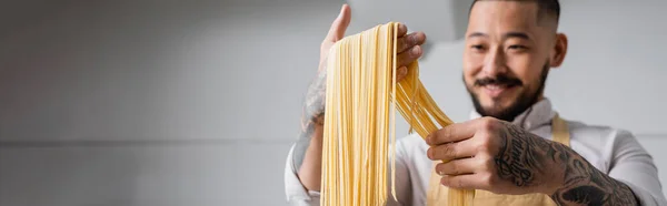 Blurred Positive Asian Chef Holding Raw Spaghetti Kitchen Banner — Stock Photo, Image