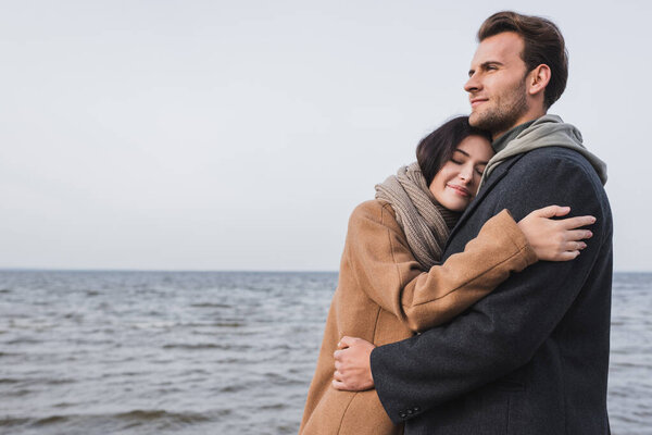 joyful woman with closed eyes embracing boyfriend near river