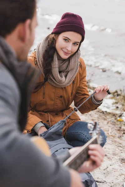 Happy Woman Opening Backpack While Looking Blurred Man Playing Guitar — Stock Photo, Image