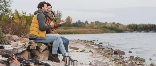 Young Couple Sandwiches Sitting Stones Blanket Thermo Cups River Shore — Stock Photo, Image