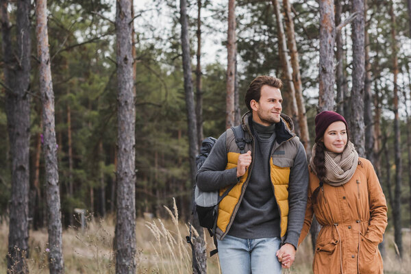 young couple in autumn outfit holding hands while hiking in forest