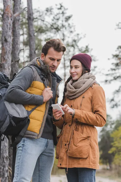 Akıllı Telefonlu Gülümseyen Kadın Ormanda Yürüyen Sırt Çantalı Adam — Stok fotoğraf