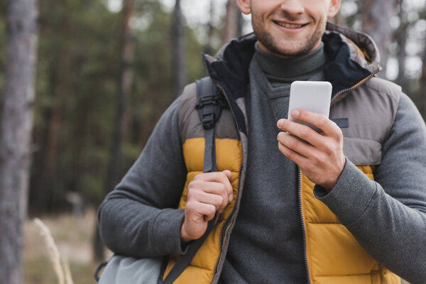 partial view of man with backpack using smartphone for navigation in forest