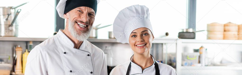 Positive chefs smiling at camera in restaurant kitchen, banner 