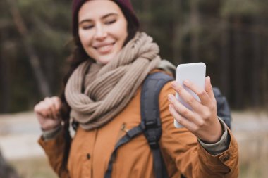 Açık havada cep telefonunda selfie çekerken gülümseyen bulanık kadın.