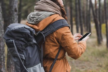 Sırt çantalı ve cep telefonlu bir kadının sonbahar ormanlarında boş ekranlı yürüyüşü.
