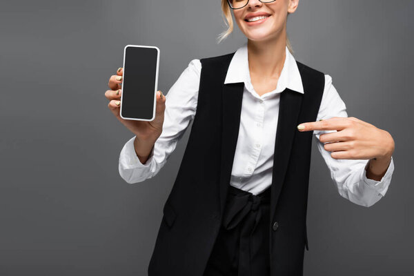 Cropped view of smiling businesswoman pointing with finger at smartphone isolated on grey 