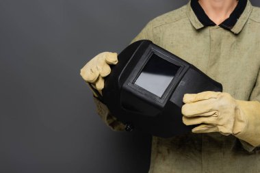 Üniformalı kaynakçı görüntüsü ve gri arka planda maske tutan eldivenler.