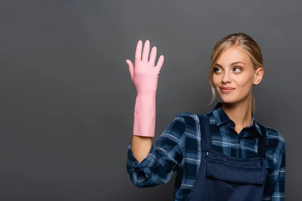 Encanador Loiro Sorridente Olhando Para Mão Luva Borracha Isolada Cinza — Fotografia de Stock