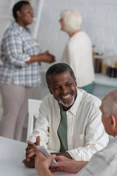 Hombre Afroamericano Sonriente Mirando Amigo Mayor Con Teléfono Inteligente Hogar — Foto de Stock