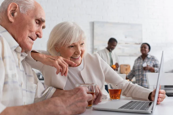 Mujer Edad Avanzada Positiva Apuntando Computadora Portátil Cerca Amigo Con — Foto de Stock