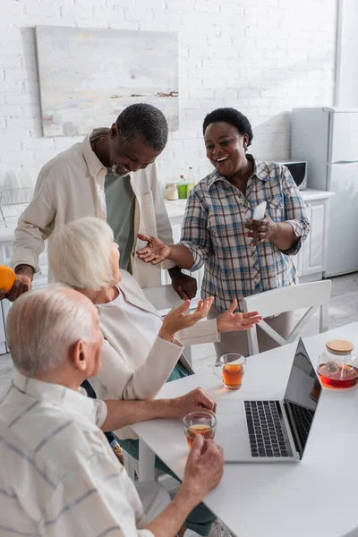 Happy African American Woman Holding Smartphone While Talking Senior Friend — Stock Photo, Image