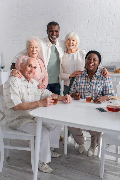 Personas Mayores Multiétnicas Positivas Abrazándose Cerca Teléfonos Inteligentes Hogar Ancianos — Foto de Stock