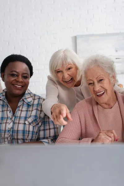 Счастливая Пожилая Женщина Указывает Ноутбук Рядом Межрасовыми Друзьями Доме Престарелых — стоковое фото