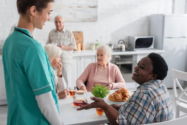 在疗养院的茶水和羊角面包旁与护士交谈的非洲裔美国妇女笑着 — 图库照片