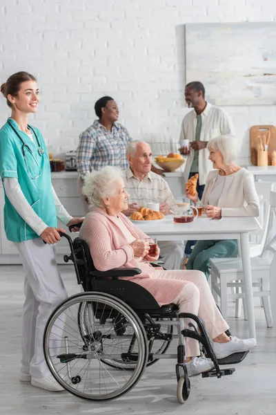 Enfermeira Sorridente Perto Mulher Idosa Cadeira Rodas Segurando Chá Casa — Fotografia de Stock