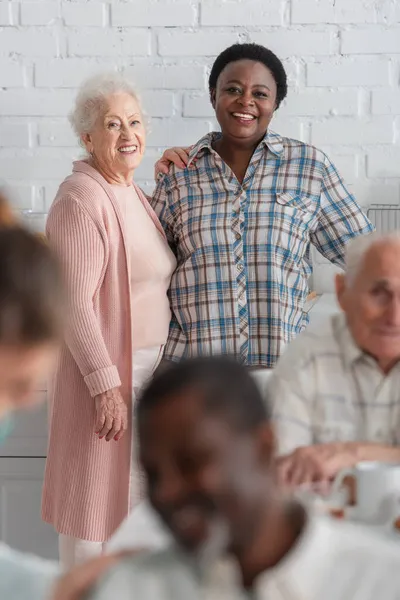 老人ホームでアフリカ系アメリカ人の友人の近くに立つ笑顔の女性 — ストック写真
