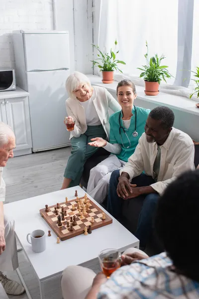 Enfermera Sonriente Apuntando Con Mano Cerca Pacientes Interracial Ajedrez Asilo — Foto de Stock