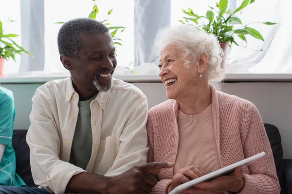 African american man pointing at digital tablet in hand of senior friend in nursing home