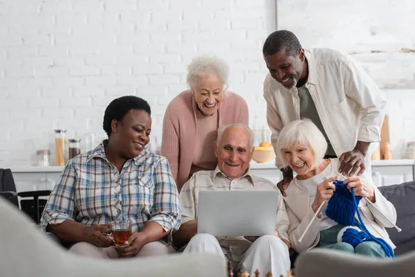 Cheerful Interracial Pensioners Yarn Tea Looking Laptop Nursing Home — Stock Photo, Image