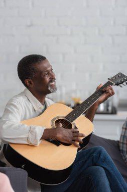 Huzurevinde akustik gitar çalan Afro-Amerikan bir adam. 
