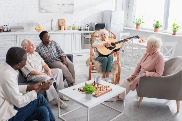 Cheerful Senior Woman Playing Acoustic Guitar Interracial Friends Chess Nursing — Stock Photo, Image