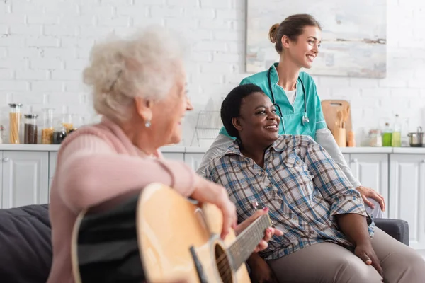 Enfermera Sonriente Mujer Afroamericana Sentada Cerca Paciente Borrosa Tocando Guitarra — Foto de Stock