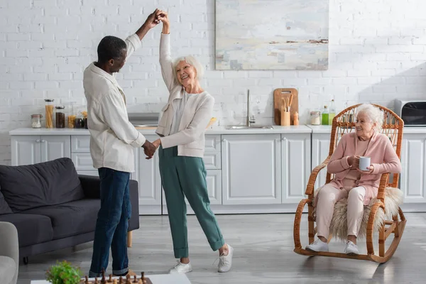 Счастливые Межрасовые Пенсионеры Танцуют Рядом Другом Чаем Кресле Качалке Доме — стоковое фото