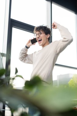 Ofiste akıllı telefonla konuşurken evet işareti yapan heyecanlı iş adamı 