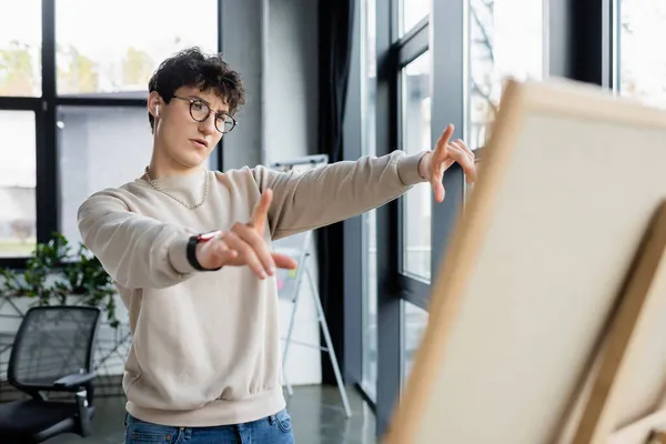 Young businessman in earphone pointing at blurred board in office