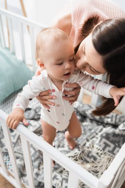 Karyolada duran esmer kadının sarılıp çocuğu öptüğü yüksek açılı manzara.