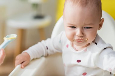 Küçük oğlu bebek koltuğunda otururken kaşıkla yemek yiyen kadın.