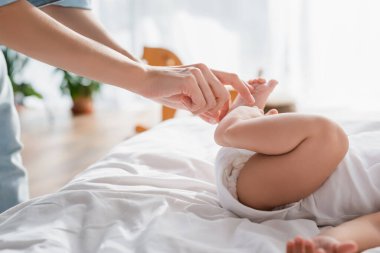 Küçük oğlunun küçük ayaklarına dokunan bir kadının yatakta uzanmış görüntüsü.