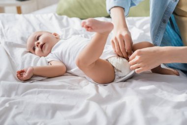Kadın küçük oğluna romper ve bebek bezi giydiriyor.