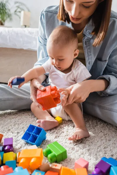 Anne ile yeni yürümeye başlayan çocuk, çok renkli yapı taşlarıyla oynuyor.