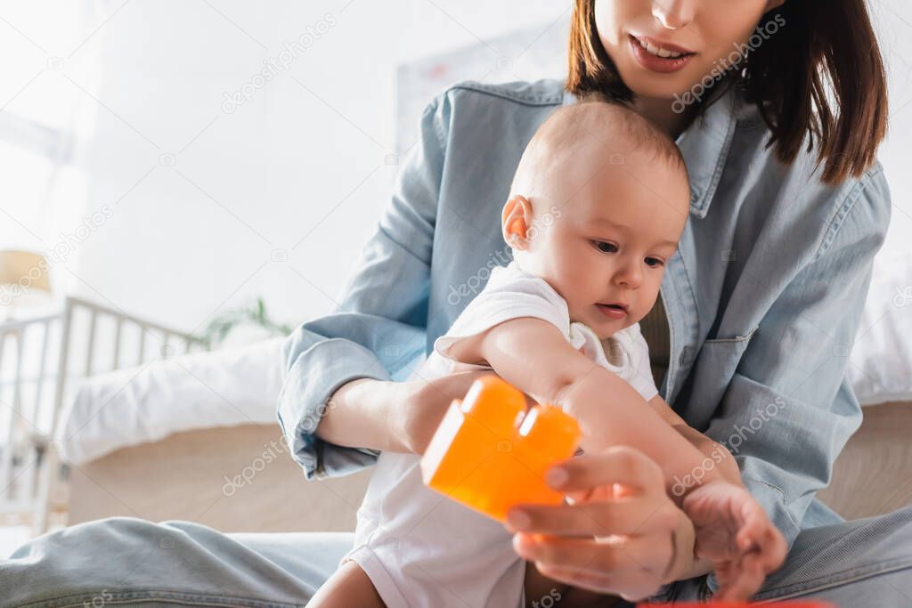 woman holding toy building block while playing with son at home