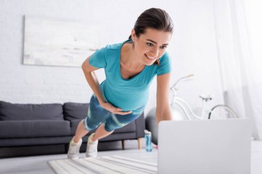 Spor kıyafetli mutlu hamile kadın oturma odasında dizüstü bilgisayarın yanında çalışıyor. 