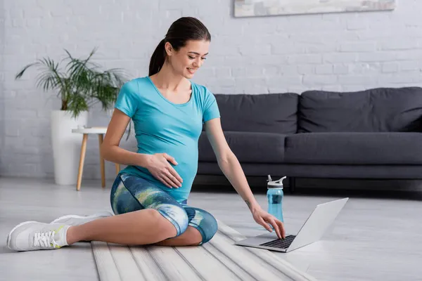 Wesoła Kobieta Ciąży Patrząc Laptopa Siedzi Macie Fitness — Zdjęcie stockowe