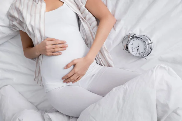 Vista Ritagliata Della Donna Incinta Vicino Sveglia Sul Letto — Foto Stock