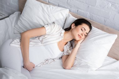 Dövmeli hamile bir kadın yatak odasında uyuyor.