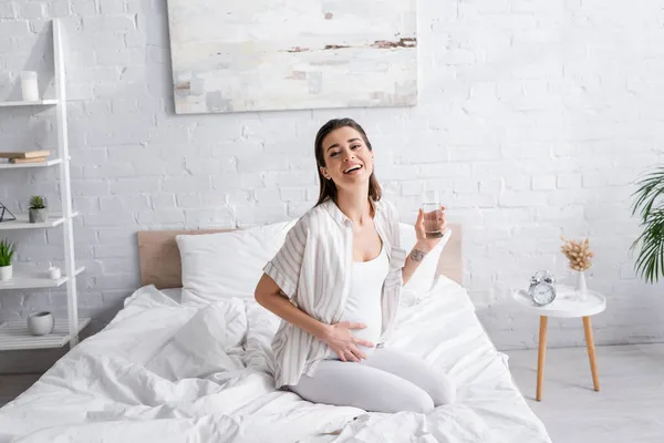 快乐的孕妇 抱着一杯水在卧室里 — 图库照片