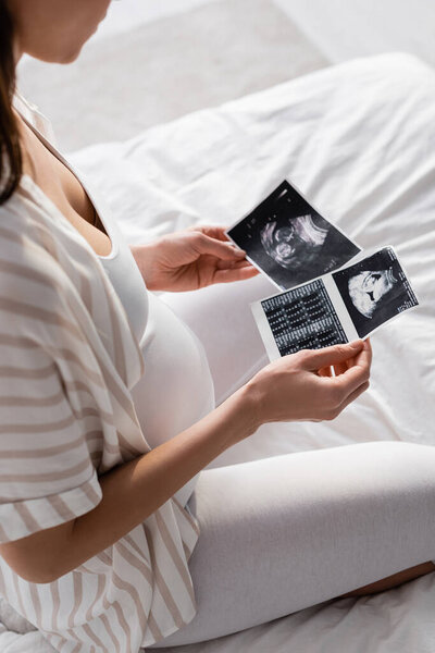 partial view of pregnant woman holding ultrasound scans 