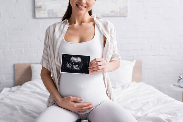 partial view of cheerful pregnant woman holding ultrasound scan 
