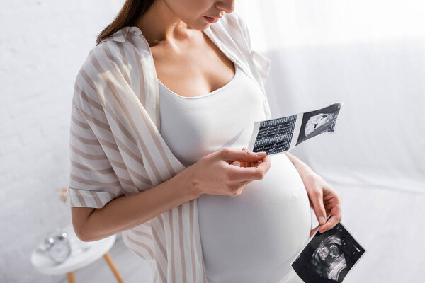 partial view of pregnant woman holding ultrasound photos 