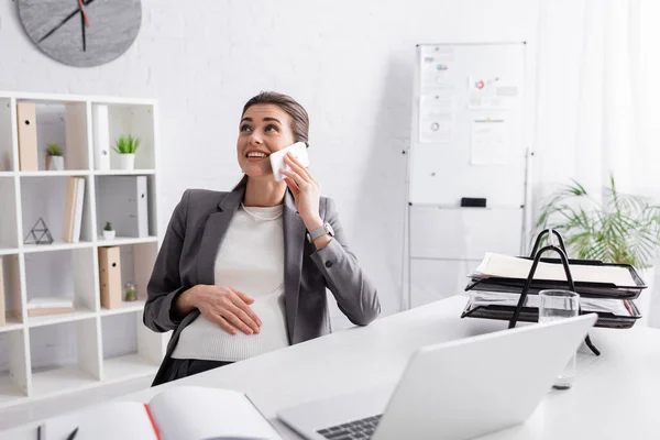 Alegre Embarazada Mujer Negocios Hablando Teléfono Inteligente Cerca Del Ordenador —  Fotos de Stock