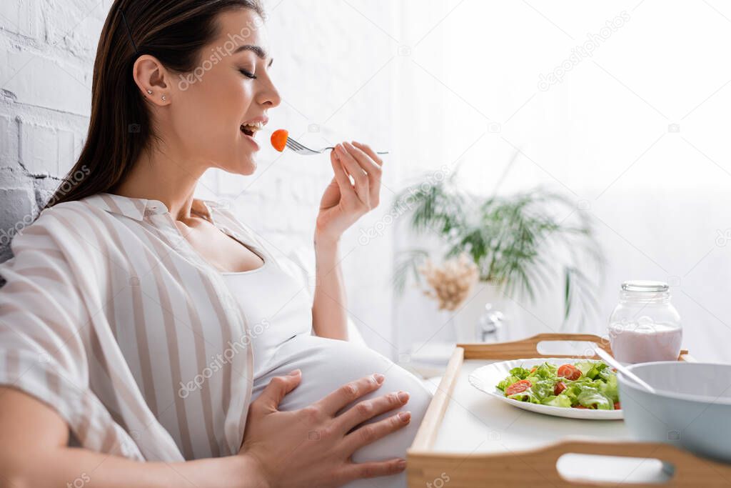 side view of happy pregnant woman holding fork with cherry tomato