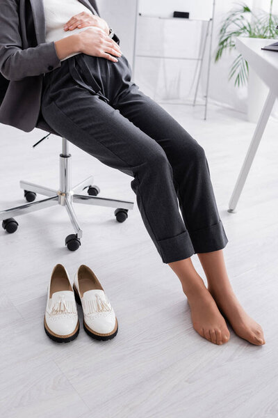 cropped view of shoeless pregnant woman sitting on chair near desk
