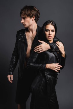 Siyah deri ceketli esmer kadına sarılan adam, gri üzerine izole edilmiş.