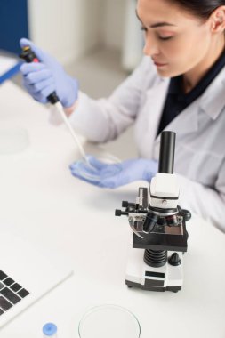 Microscope near laptop and blurred scientist working in lab  clipart