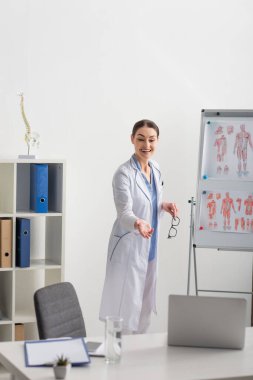 Görüntülü arama sırasında gülümseyen doktor anatomi resimleriyle birlikte ters yüz çizelgesinin yanında dururken